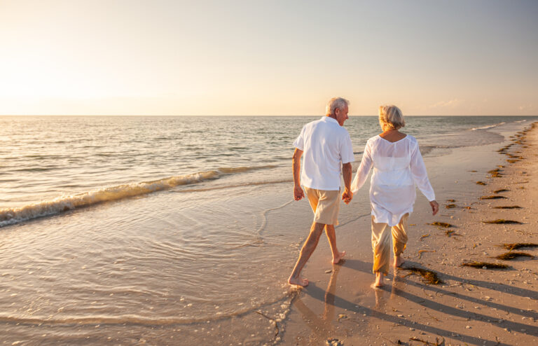 Happy senior couple walking and holding hands on a beach.